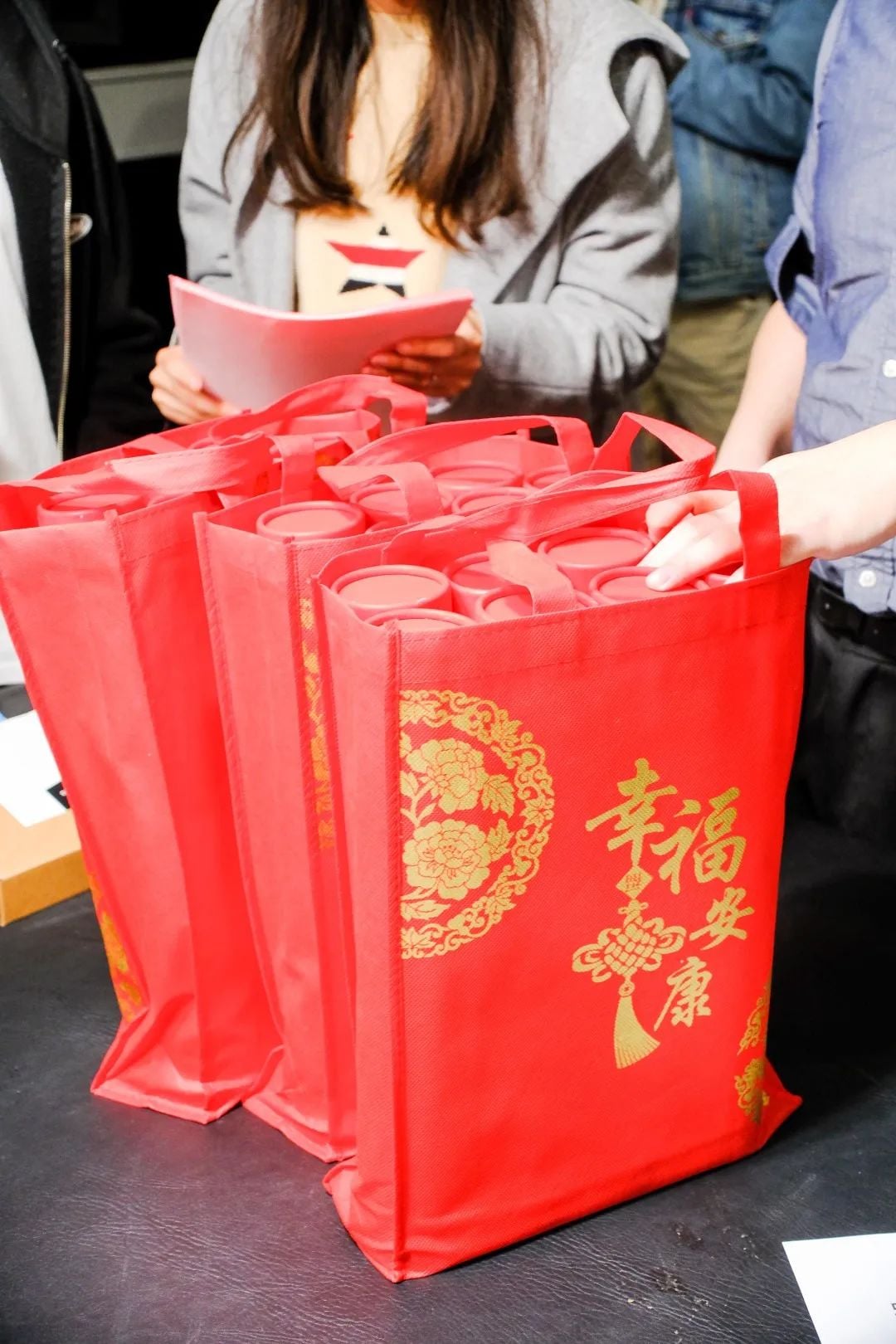 红色袋子,上面有金色中文字和花纹,里面装有圆柱形物品,背景有人。