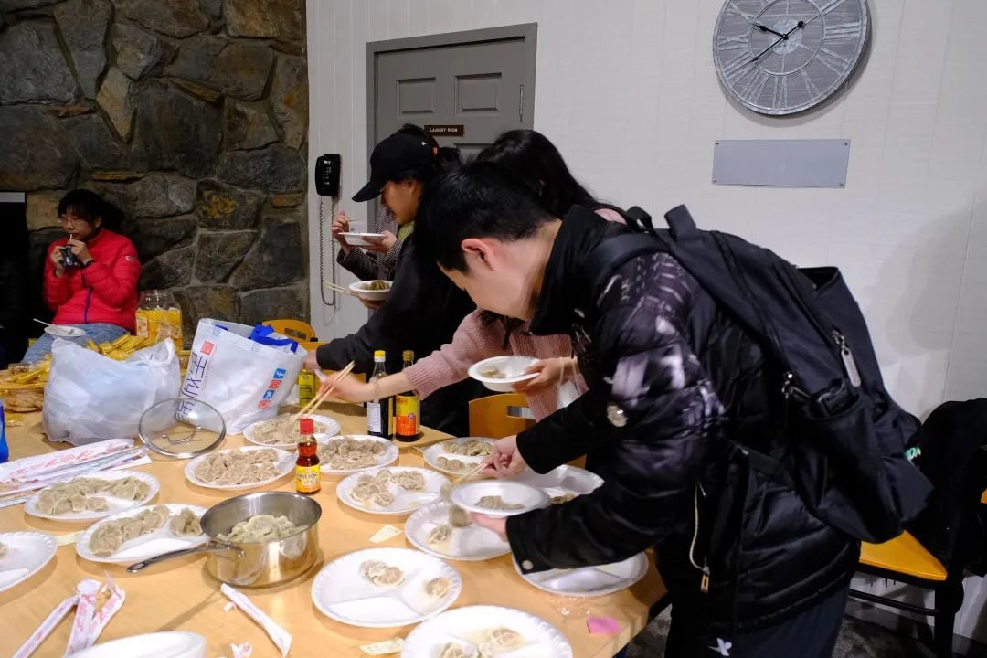 人们围着摆满饺子和酱料的桌子,正在盛取和享用食物。