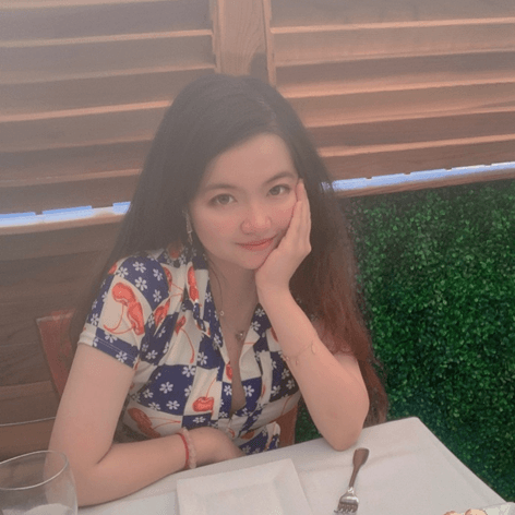 一位长发女性身穿花衬衫,手托下巴坐在餐桌旁微笑。