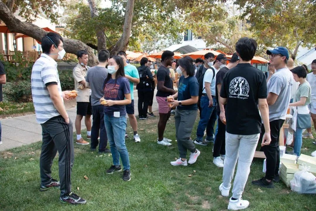 一群人戴着口罩在草地上户外聚会,手里拿着食物。