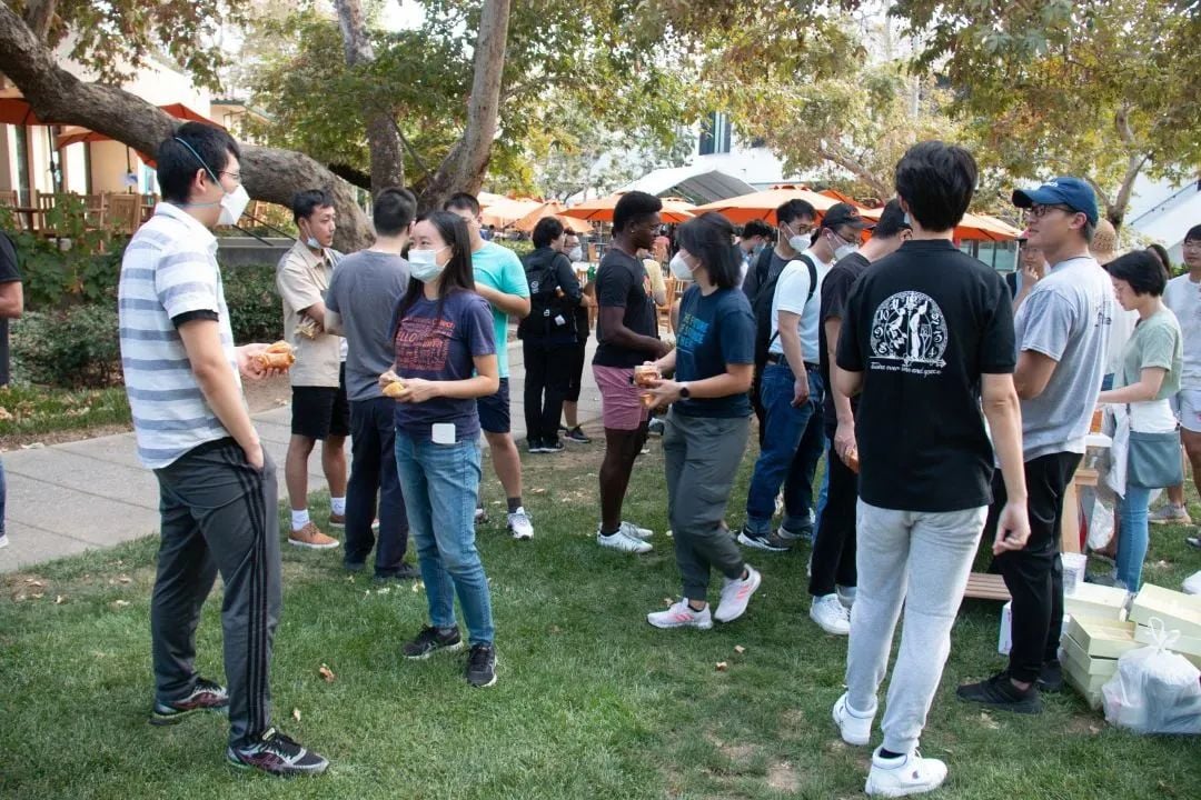 一群人戴着口罩在草地上户外聚会,手里拿着食物。